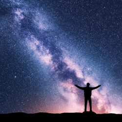 Milky Way and silhouette of a standing happy man with raised up arms. Travel in Nepal. Landscape with beautiful galaxy. Universe. Night sky with stars, colorful Milky Way. Starry sky and man. Space